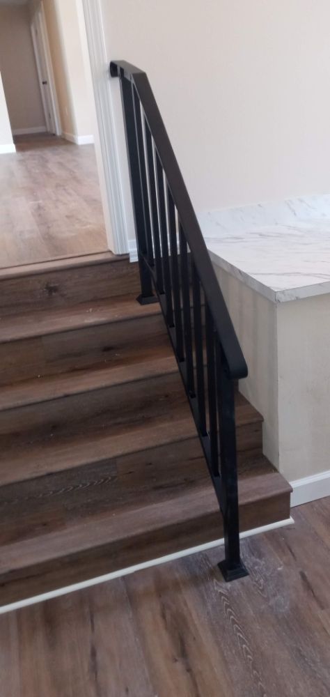 Black iron stair railing on hardwood stairs with marble accent wall
